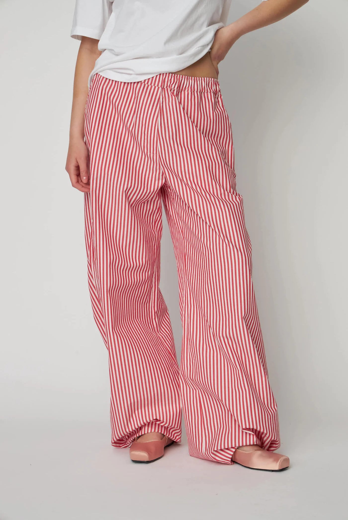 Oversizowe, bawełniane spodnie w czerwono-białe paski Oversized Striped STELLA NOVA z szerokimi i długimi nogawkami ściąganymi u dołu za pomocą gumek. Spodnie mają wysoki stan i elastyczną talię.