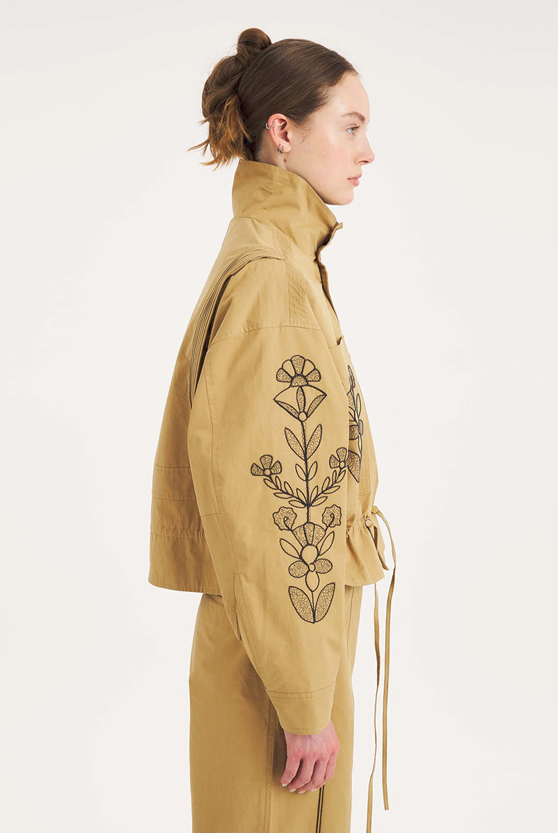 Krótka, strukturalna kurtka Maria Beige Antik Batik o nowoczesnym, nieco geometrycznym kroju. Posiada charakterystyczną, bardzo wysoką stójkę zapinaną na guziki. Regulowana w pasie za pomocą ściągacza ze sznurkami, co tworzy efekt delikatnej baskinki/falbany. Z przodu na kieszeniach oraz na rękawach znajdują się hafty z motywami roślinnymi i kwiatowymi. Dodatkowe, drobne, haftowane przeszycia ozdabiają również linię ramion. Zapinana na guziki.
-Krótki, nowoczesny fason
-Hafty z motywami roślinnymi i