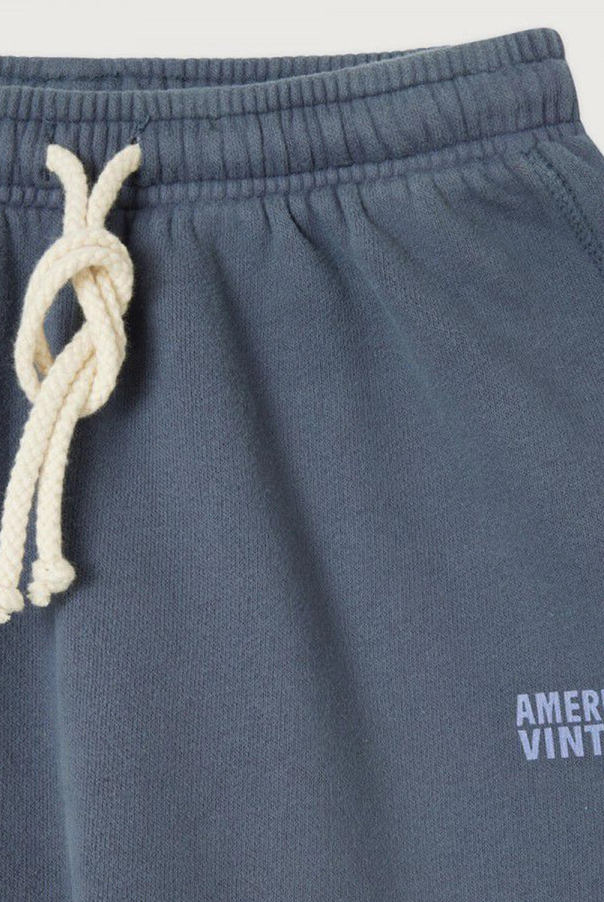 Luźne, bawełniane spodnie dresowe IZUBIRD American Vintage z wysokim stanem i szeroką, lekko skróconą nogawką. Wiązane i elastyczne w talii. Na lewej nogawce spodnie mają niewielkie logo marki.