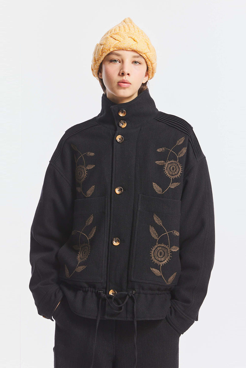 Kurtka o kroju oversize Aristide Antik Batik Grey z wysokim kołnierzem i zapięciem na guziki. Wykonana z mieszanki bawełny, wełny i nylonu. Model ten wyróżnia się strukturalną formą i swobodnym ułożeniem na sylwetce. Przód zdobią delikatne, kwiatowe hafty, które nadają kurtce fakturę i charakter. Posiada dwie naszywane kieszenie i dwie kieszenie boczne. Regulowany u dołu sznurek pozwala na dowolne podkreślenie sylwetki. Model wykończony podszewką z lyocellu. 