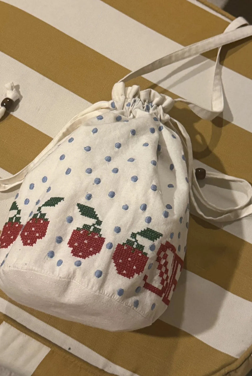 Torebka na ramię Babba Drawstring Off White marki SISSEL EDELBO z bawełny organicznej. Zmieścisz w niej niezbędne rzeczy na co dzień. Ma okrągłe dno i można ją zamknąć za pomocą sznurków. Ozdobiona jest uroczymi, niebieskimi kropkami i haftem krzyżykowym wzdłuż dolnej krawędzi, a także małym, haftowanym napisem SE.