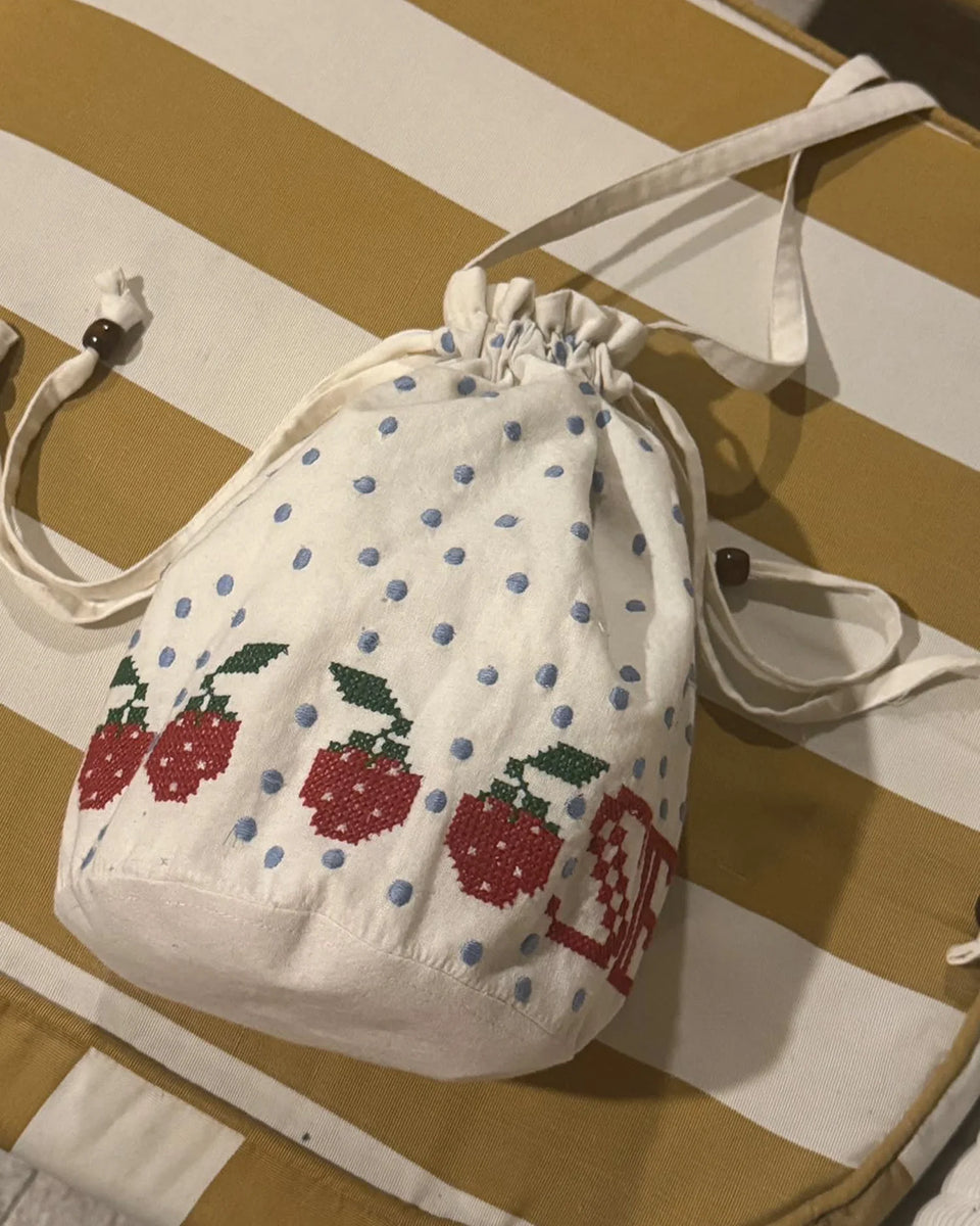 Torebka na ramię Babba Drawstring Off White marki SISSEL EDELBO z bawełny organicznej. Zmieścisz w niej niezbędne rzeczy na co dzień. Ma okrągłe dno i można ją zamknąć za pomocą sznurków. Ozdobiona jest uroczymi, niebieskimi kropkami i haftem krzyżykowym wzdłuż dolnej krawędzi, a także małym, haftowanym napisem SE.