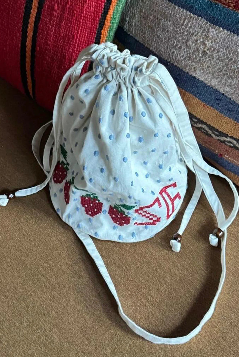 Torebka na ramię Babba Drawstring Off White marki SISSEL EDELBO z bawełny organicznej. Zmieścisz w niej niezbędne rzeczy na co dzień. Ma okrągłe dno i można ją zamknąć za pomocą sznurków. Ozdobiona jest uroczymi, niebieskimi kropkami i haftem krzyżykowym wzdłuż dolnej krawędzi, a także małym, haftowanym napisem SE.