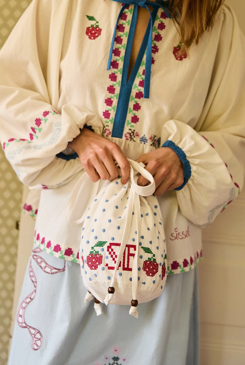 Torebka na ramię Babba Drawstring Off White marki SISSEL EDELBO z bawełny organicznej. Zmieścisz w niej niezbędne rzeczy na co dzień. Ma okrągłe dno i można ją zamknąć za pomocą sznurków. Ozdobiona jest uroczymi, niebieskimi kropkami i haftem krzyżykowym wzdłuż dolnej krawędzi, a także małym, haftowanym napisem SE.