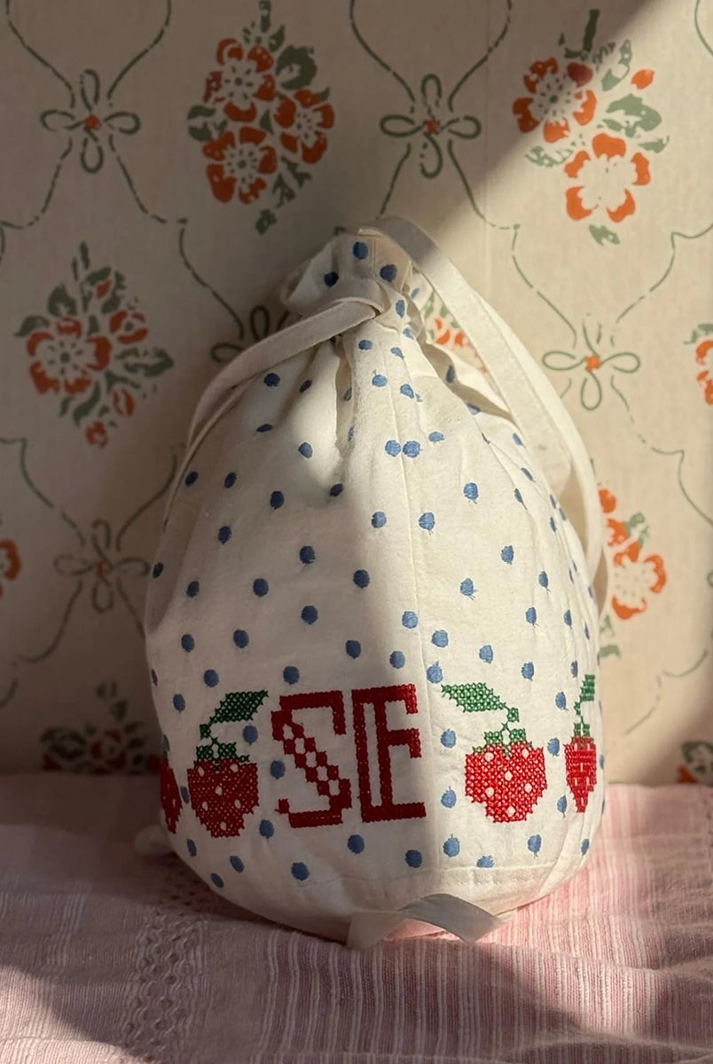 Torebka na ramię Babba Drawstring Off White marki SISSEL EDELBO z bawełny organicznej. Zmieścisz w niej niezbędne rzeczy na co dzień. Ma okrągłe dno i można ją zamknąć za pomocą sznurków. Ozdobiona jest uroczymi, niebieskimi kropkami i haftem krzyżykowym wzdłuż dolnej krawędzi, a także małym, haftowanym napisem SE.