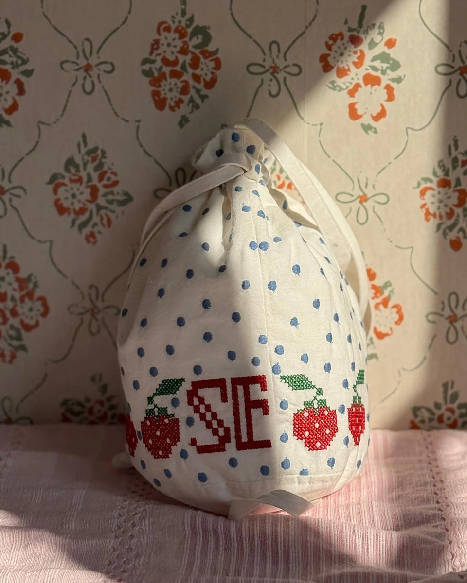 Torebka na ramię Babba Drawstring Off White marki SISSEL EDELBO z bawełny organicznej. Zmieścisz w niej niezbędne rzeczy na co dzień. Ma okrągłe dno i można ją zamknąć za pomocą sznurków. Ozdobiona jest uroczymi, niebieskimi kropkami i haftem krzyżykowym wzdłuż dolnej krawędzi, a także małym, haftowanym napisem SE.