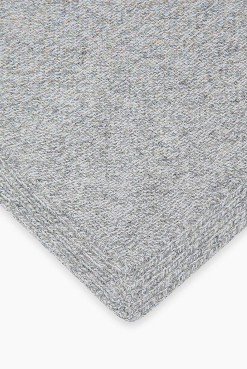 Dzianinowy, szary szalik Breeze Bandana Light Grey Melange w kształcie bandany. Składa się z trójkątnej części głównej z dłuższymi troczkami zaprojektowanymi do owinięcia pod szyją, co pozwala na naturalne i schludne układanie się materiału. Wykonany z 90% wełny merino oraz 10% kaszmiru, co zapewnia mu miękkość i ciepło. 