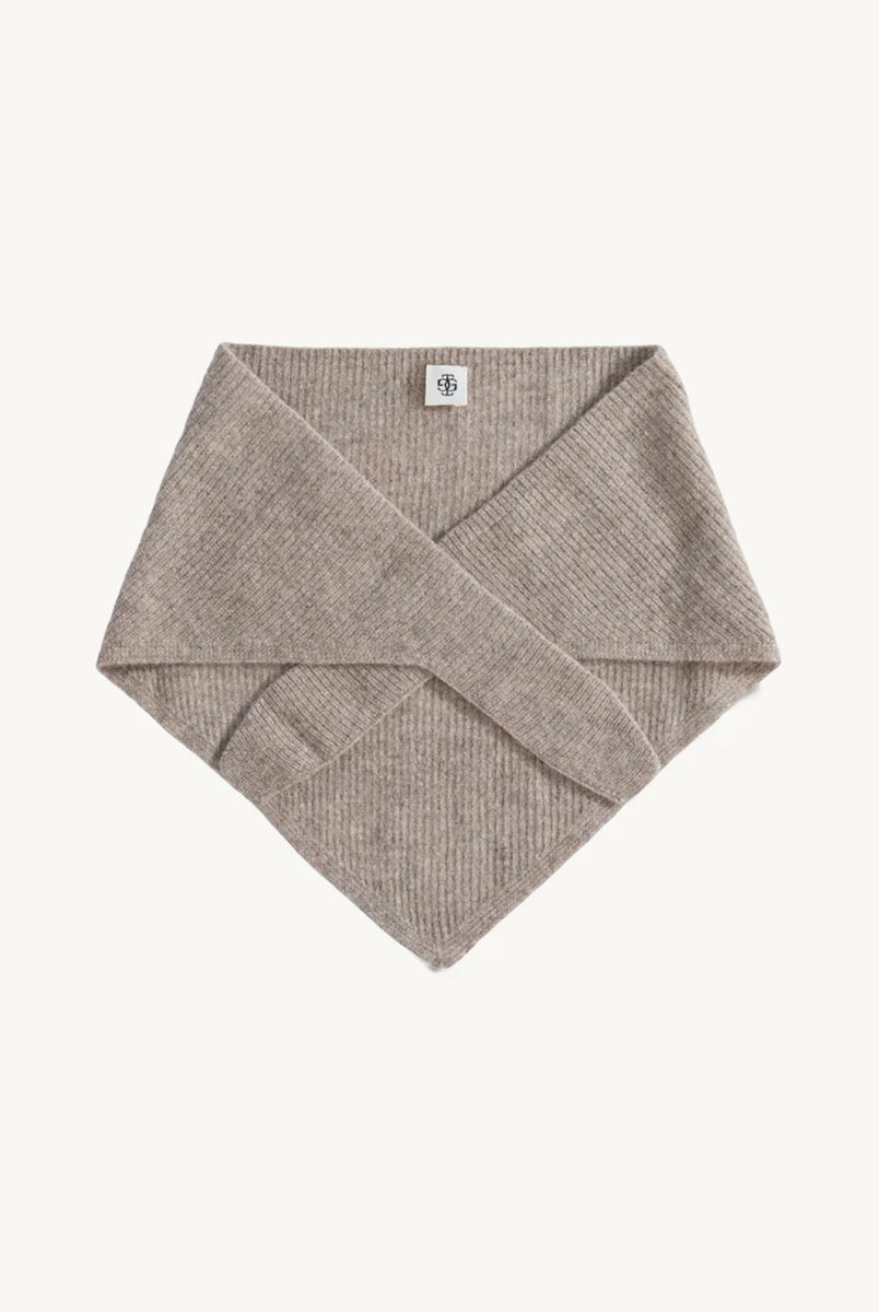 Dzianinowy, beżowy szalik Como Bandana Scarf w kształcie bandany, który charakteryzuje się gładką strukturą. Składa się z trójkątnej części głównej z dłuższymi troczkami zaprojektowanymi do owinięcia pod szyją, co pozwala na naturalne i schludne układanie się materiału. Wykonany z 95% wełny oraz 5% kaszmiru, co zapewnia mu miękkość i ciepło. 