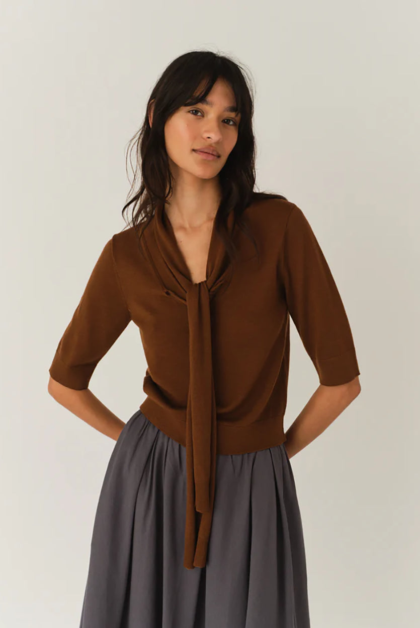 Cienki, brązowy sweter Bergen Scarf Cinnamon o dopasowanym kroju, z elastycznym ściagaczem w pasie i przy zakończeniach rękawów. Rękawy są długości do łokcia. Dekolt jest w nieco głębszy i okrągły z doszytym długim szalem, który można puścić luźno lub dowolnie związać. Wykonany w 100% z wełny merino.