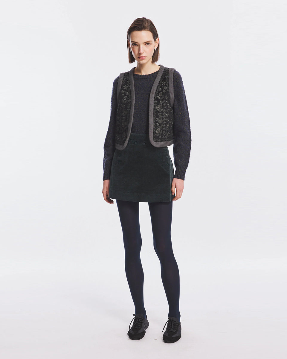 Krótka kamizelka Bertille Black marki Antik Batik o wyraźnym, etnicznym charakterze nawiązującym do stylu boho-chic. Jest to fason sięgający do linii bioder, z otwartym przodem, bez widocznego zapięcia. Przód kamizelki zdobi bogaty, symetryczny haft. Wykonana z mieszanki wełny i bawełny. Wszystkie krawędzie zostały obszyte ozdobną, wzorzystą taśmą z geometrycznym haftem. Zestaw ją z ulubionymi spodniami oraz luźną, białą koszulą z bufiastymi rękawami i wysoką stójką. 