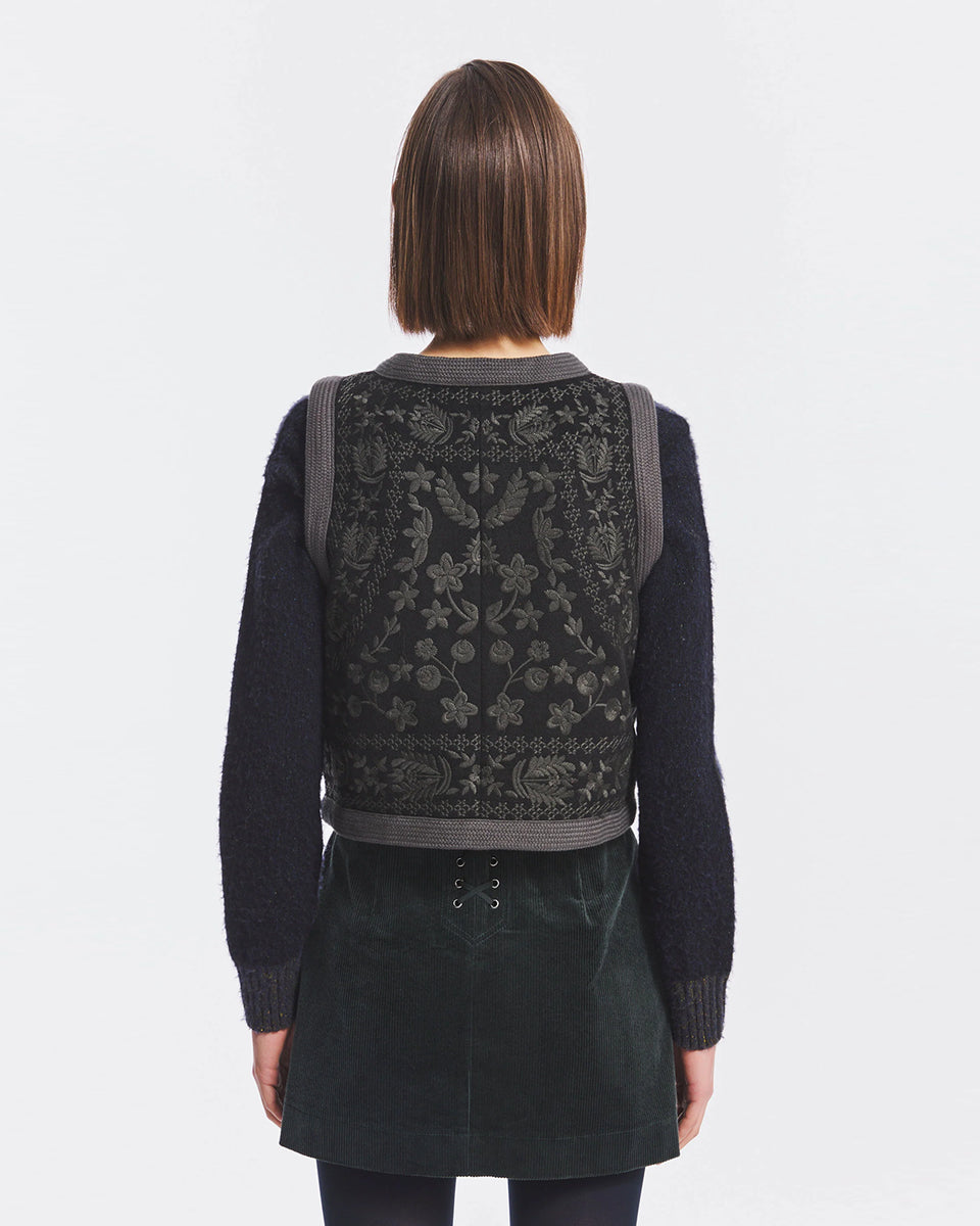 Krótka kamizelka Bertille Black marki Antik Batik o wyraźnym, etnicznym charakterze nawiązującym do stylu boho-chic. Jest to fason sięgający do linii bioder, z otwartym przodem, bez widocznego zapięcia. Przód kamizelki zdobi bogaty, symetryczny haft. Wykonana z mieszanki wełny i bawełny. Wszystkie krawędzie zostały obszyte ozdobną, wzorzystą taśmą z geometrycznym haftem. Zestaw ją z ulubionymi spodniami oraz luźną, białą koszulą z bufiastymi rękawami i wysoką stójką. 
