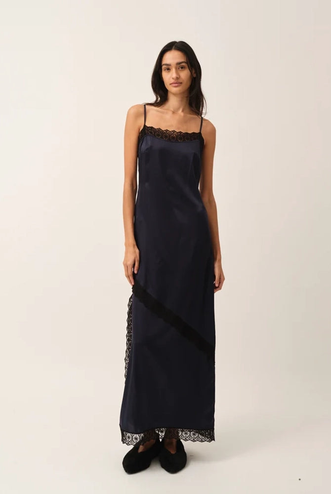 Elegancka, lejąca sukienka maxi na cienkich, regulowanych ramiączkach Cata Lace The Garment wykończona zmysłową koronką. Posiada prosty dekolt i głębokie wycięcie na plecach. Z przodu dekorowana asymetryczną koronką. Sukienka ma boczne rozcięcie oraz długość do kostek. Z tyłu delikatnie drapowana. Wykonana z jedwabnej, śliskiej tkaniny.
