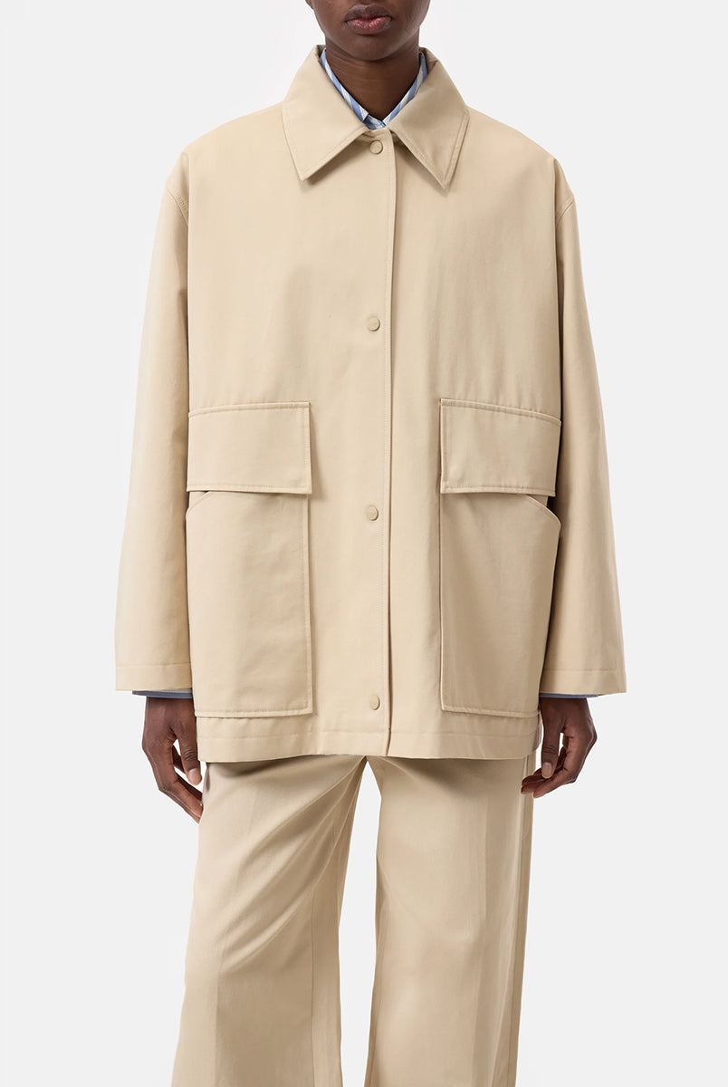 Cienki, krótki, beżowy płaszcz Short coat 97949 CLOSED o luźnym fasonie i prostym kroju. Posiada szerokie, długie rękawy, kołnierzyk i duże, przednie kieszenie z klapkami. Zapinany za pomocą zatrzaskowych guzików