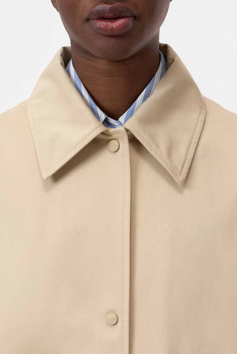 Cienki, krótki, beżowy płaszcz Short coat 97949 CLOSED o luźnym fasonie i prostym kroju. Posiada szerokie, długie rękawy, kołnierzyk i duże, przednie kieszenie z klapkami. Zapinany za pomocą zatrzaskowych guzików