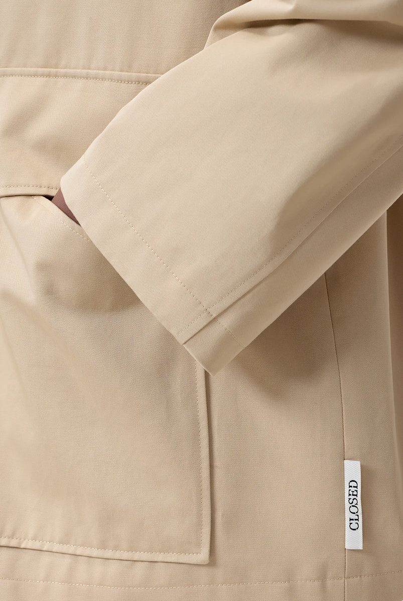 Cienki, krótki, beżowy płaszcz Short coat 97949 CLOSED o luźnym fasonie i prostym kroju. Posiada szerokie, długie rękawy, kołnierzyk i duże, przednie kieszenie z klapkami. Zapinany za pomocą zatrzaskowych guzików