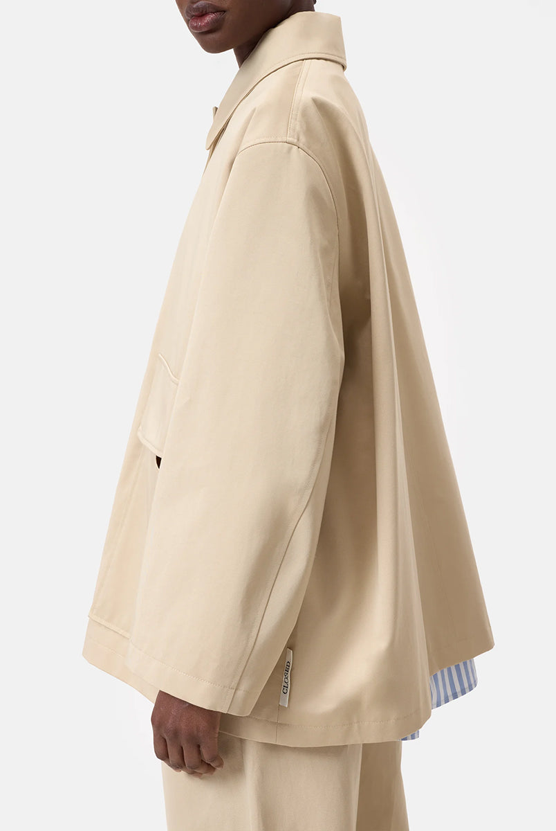 Cienki, krótki, beżowy płaszcz Short coat 97949 CLOSED o luźnym fasonie i prostym kroju. Posiada szerokie, długie rękawy, kołnierzyk i duże, przednie kieszenie z klapkami. Zapinany za pomocą zatrzaskowych guzików
