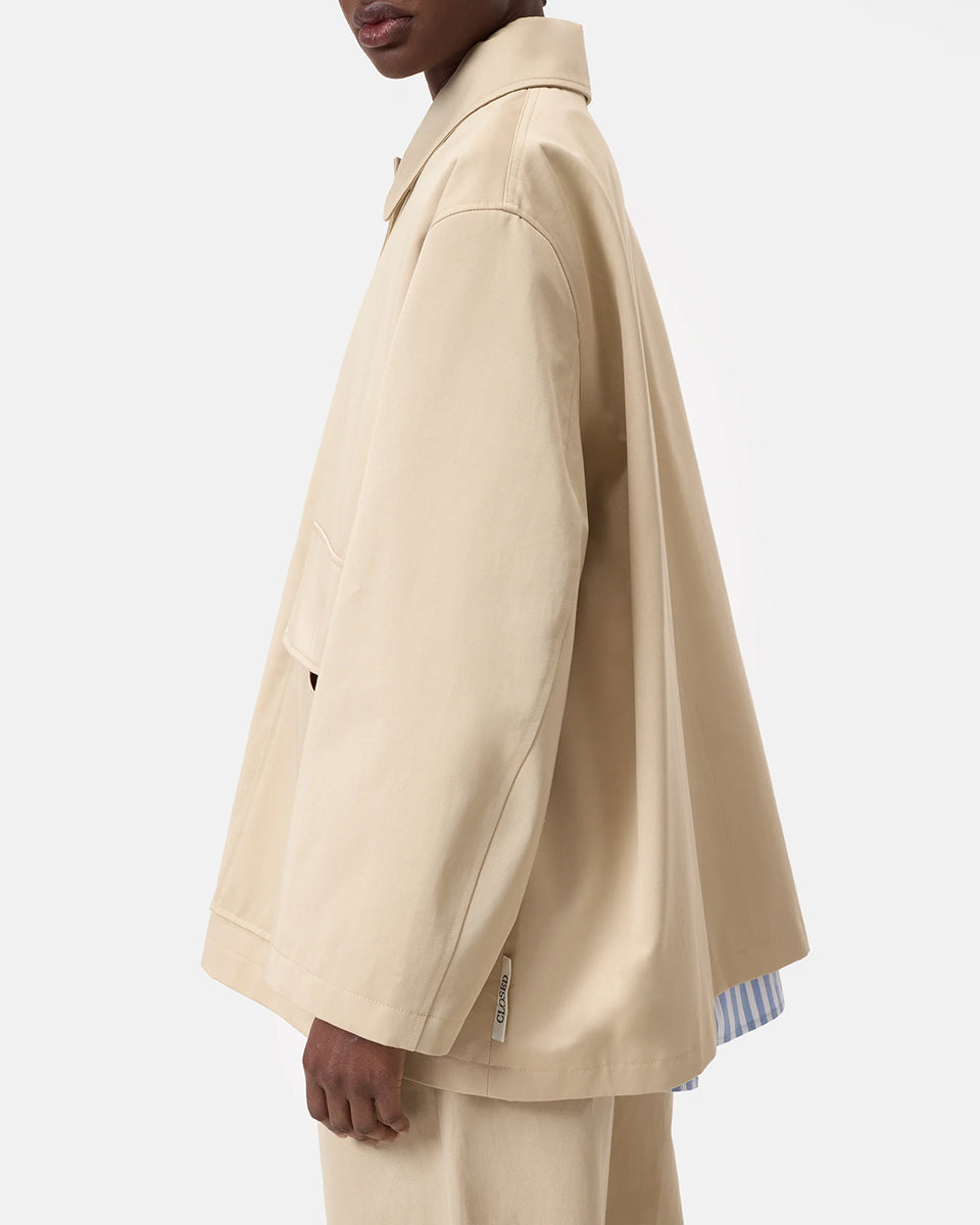 Cienki, krótki, beżowy płaszcz Short coat 97949 CLOSED o luźnym fasonie i prostym kroju. Posiada szerokie, długie rękawy, kołnierzyk i duże, przednie kieszenie z klapkami. Zapinany za pomocą zatrzaskowych guzików