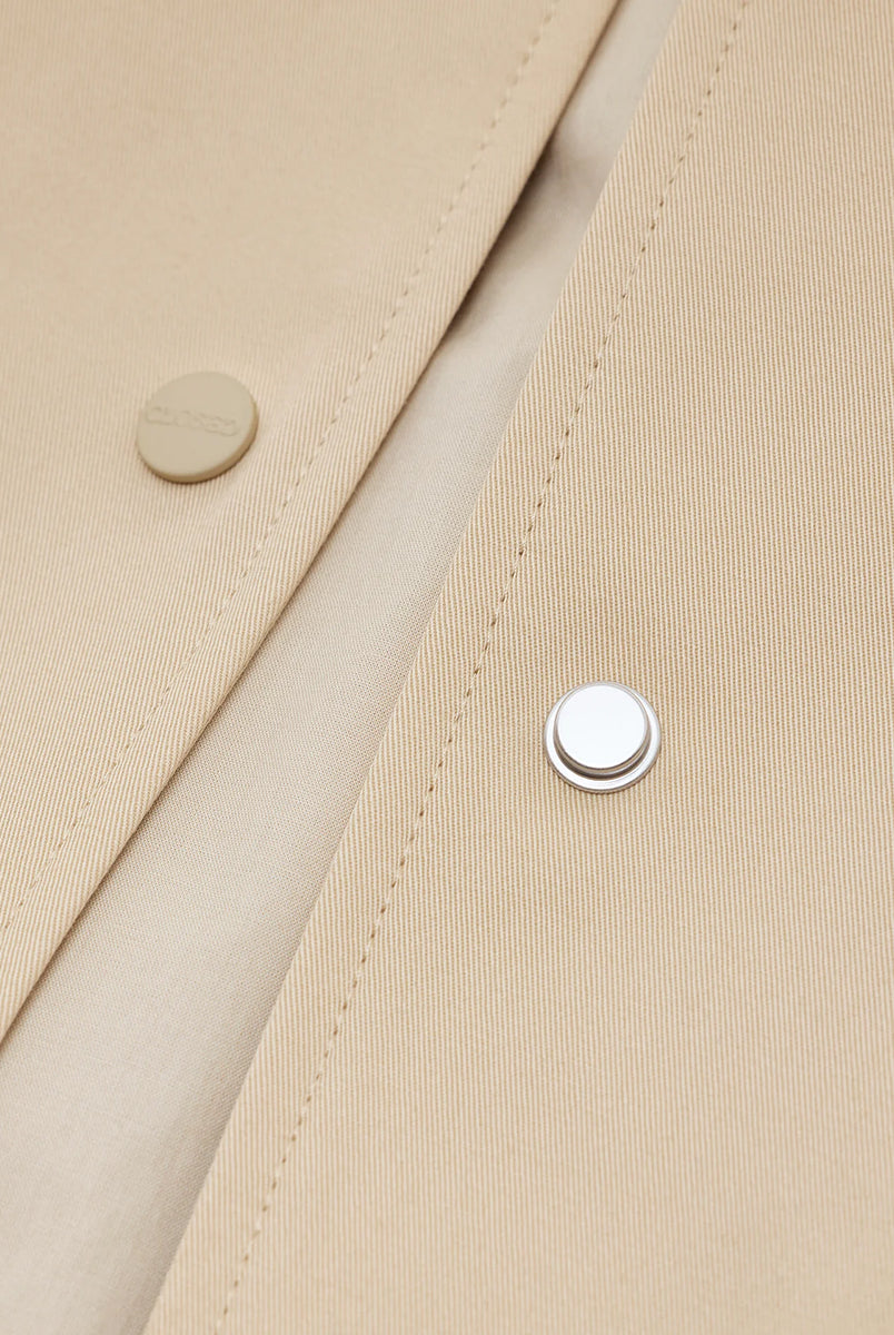 Cienki, krótki, beżowy płaszcz Short coat 97949 CLOSED o luźnym fasonie i prostym kroju. Posiada szerokie, długie rękawy, kołnierzyk i duże, przednie kieszenie z klapkami. Zapinany za pomocą zatrzaskowych guzików
