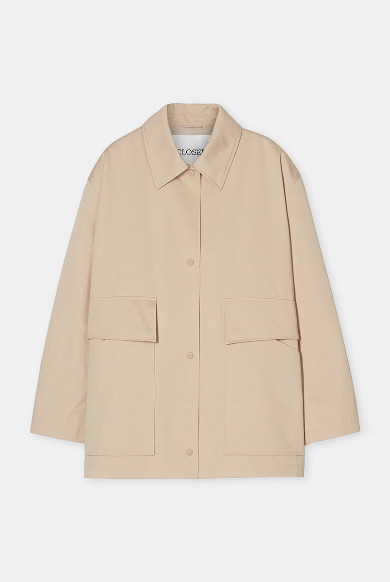 Cienki, krótki, beżowy płaszcz Short coat 97949 CLOSED o luźnym fasonie i prostym kroju. Posiada szerokie, długie rękawy, kołnierzyk i duże, przednie kieszenie z klapkami. Zapinany za pomocą zatrzaskowych guzików