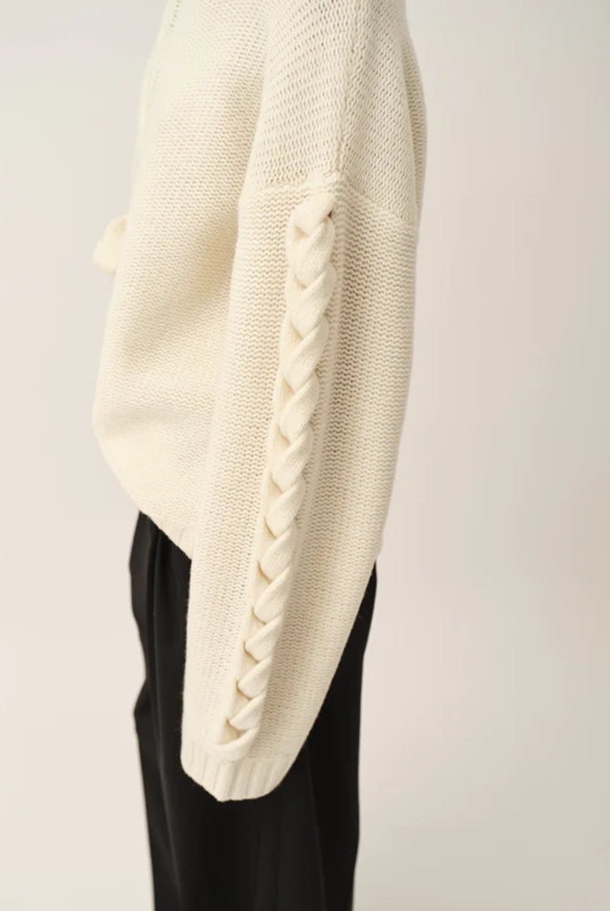Luźny, gruby, kremowy golf Como Braid The Garment z pięknymi, warkoczowymi i wzorami. Posiada opadające ramiona i szeroki, zaokrąglone rękawy. Wykończony ściągaczami o prążkowanej fakturze. Sweter ma długość za biodra. Wykonany bardzo ciepłej i miękkiej, wełnianej dzianiny z kaszmirem.