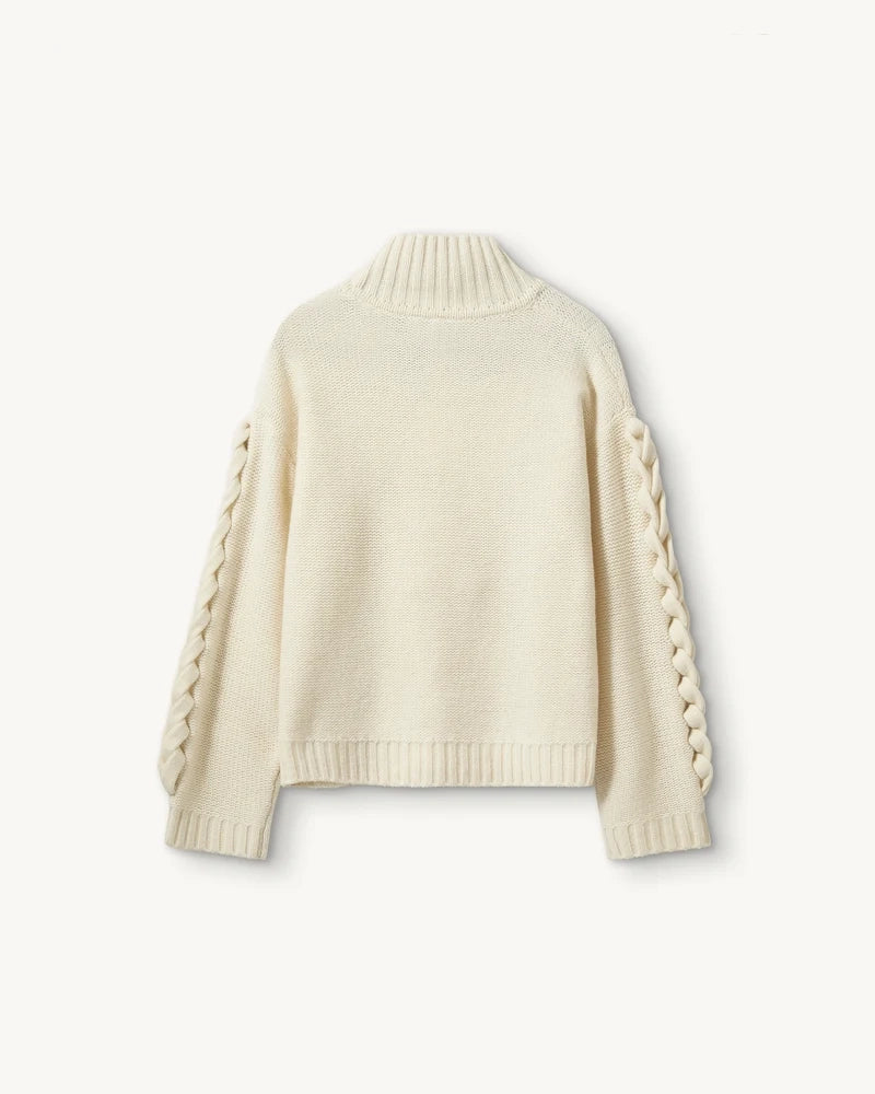 Luźny, gruby, kremowy golf Como Braid The Garment z pięknymi, warkoczowymi i wzorami. Posiada opadające ramiona i szeroki, zaokrąglone rękawy. Wykończony ściągaczami o prążkowanej fakturze. Sweter ma długość za biodra. Wykonany bardzo ciepłej i miękkiej, wełnianej dzianiny z kaszmirem.