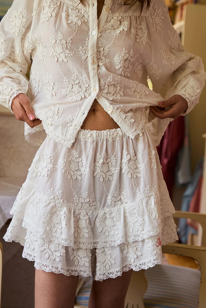 Falbaniaste, kobiece szorty Delphine Off White marki SISSEL EDELBO z elastycznym pasem. Wzdłuż bioder i nogawek ozdobione są falbanami zakończonymi delikatnymi, koronkowymi tasiemkami. Z przodu posiadają haftowany napis 'SISSEL'. Wykonane z bawełny schiffli, zgodnie z ideą marki wykorzystując różnego rodzaju resztki tkanin zamiast produkcji nowych.
-ONE SIZE