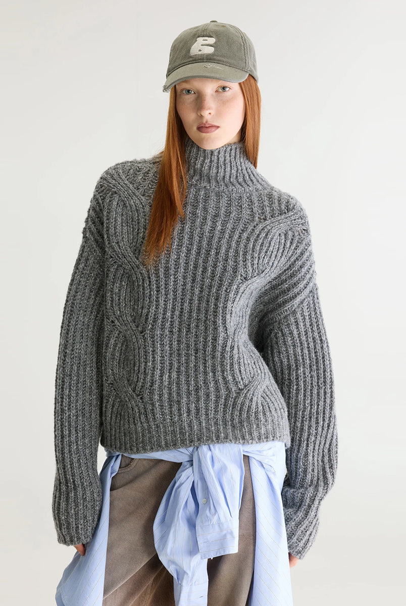 Szary sweter z golfem Deteo Mid Grey marki Bellerose o kroju oversize. Wykonany ściegiem typu "full cardigan", wyróżnia się bardzo grubym splotem ściągaczowym oraz dużymi wzorami warkoczowymi korpusie i rękawach.
-Krój oversize: celowo powiększony fason zapewniający obszerną, luźną sylwetkę
-Golf
-Warkoczowy splot 