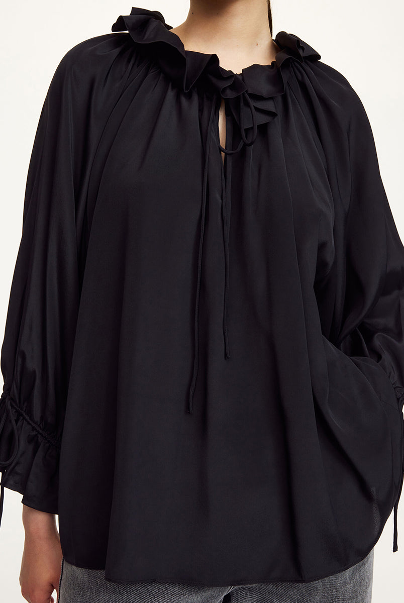 Oversizowa, lekka bluzka Dicte Black By Malene Birger z szerokimi rękawami 7/8, które zakończone są efektowną falbaną oraz ściągaczem, co tworzy delikatny efekt "bombki". Posiada kołnierz ze stójką z gęstym marszczeniem i falbaną. Dekolt jest rozcięty i posiada troczki, które można związać lub pozostawić luźno. Dół wykończony na prosto pozwala nosić bluzkę zarówno wypuszczoną, jak i luźno wpuszczoną w spodnie.
-Zamów w swoim standardowym rozmiarze