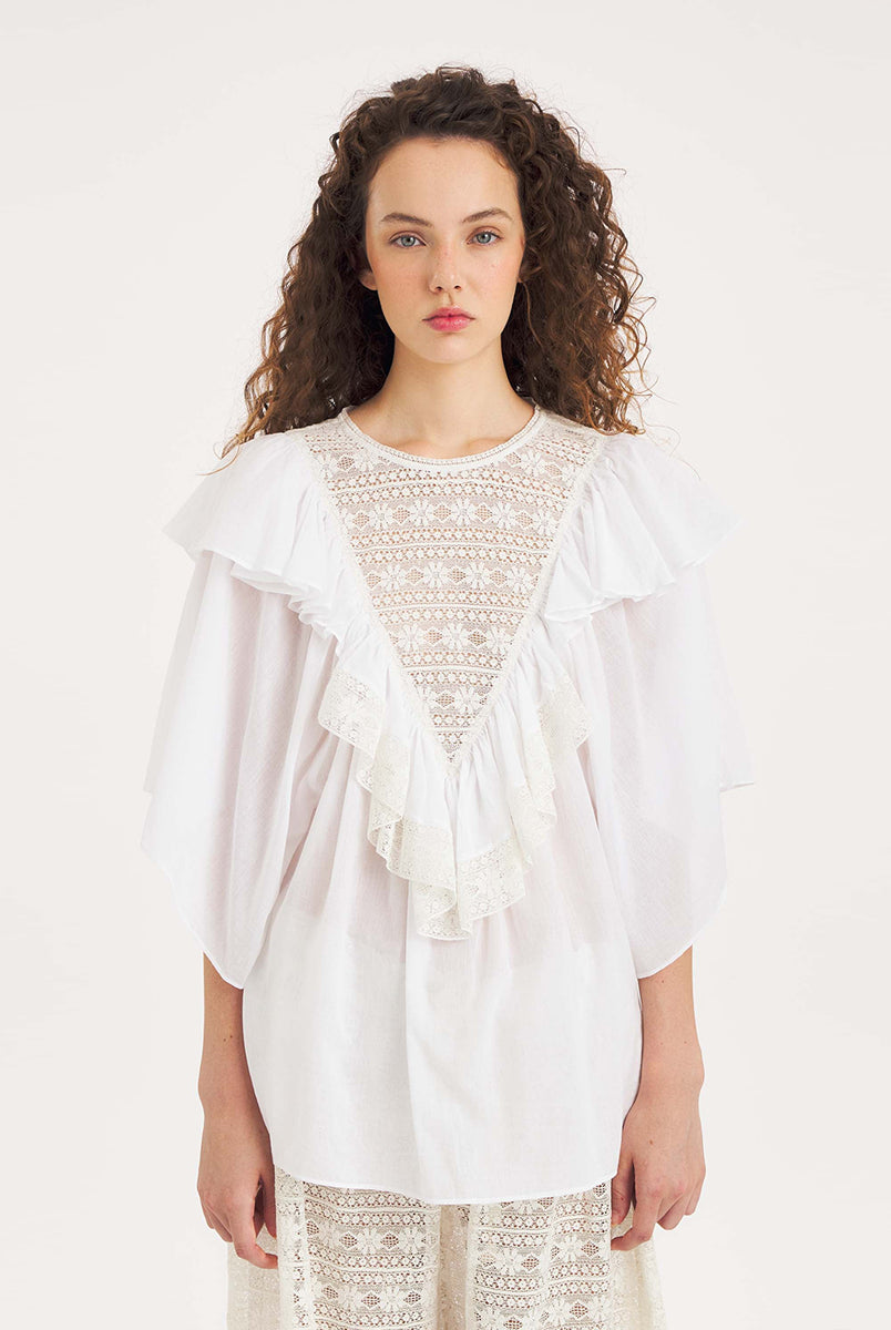 Luźna, biała bluzka Dolly White marki Antik Batik o swobodnym kroju, wyróżniającą się mocno romantycznym stylem boho. Z przodu jak i z tyłu posiada duży, ażurowy panel z misternej koronki o geometryczno- kwiatowym wzorze, który układa się w kształt litery V. Koronkowy dekolt zakończony jest szerokimi falbanami, które płynnie przechodzą w luźne, motylkowe rękawy o długości do łokcia. Z tyłu bluzka posiada subtelne rozcięcie w łezkę zapinane na guzik.
-Swobodny, luźny fason
-Falbany
-Koronka
-Zamów