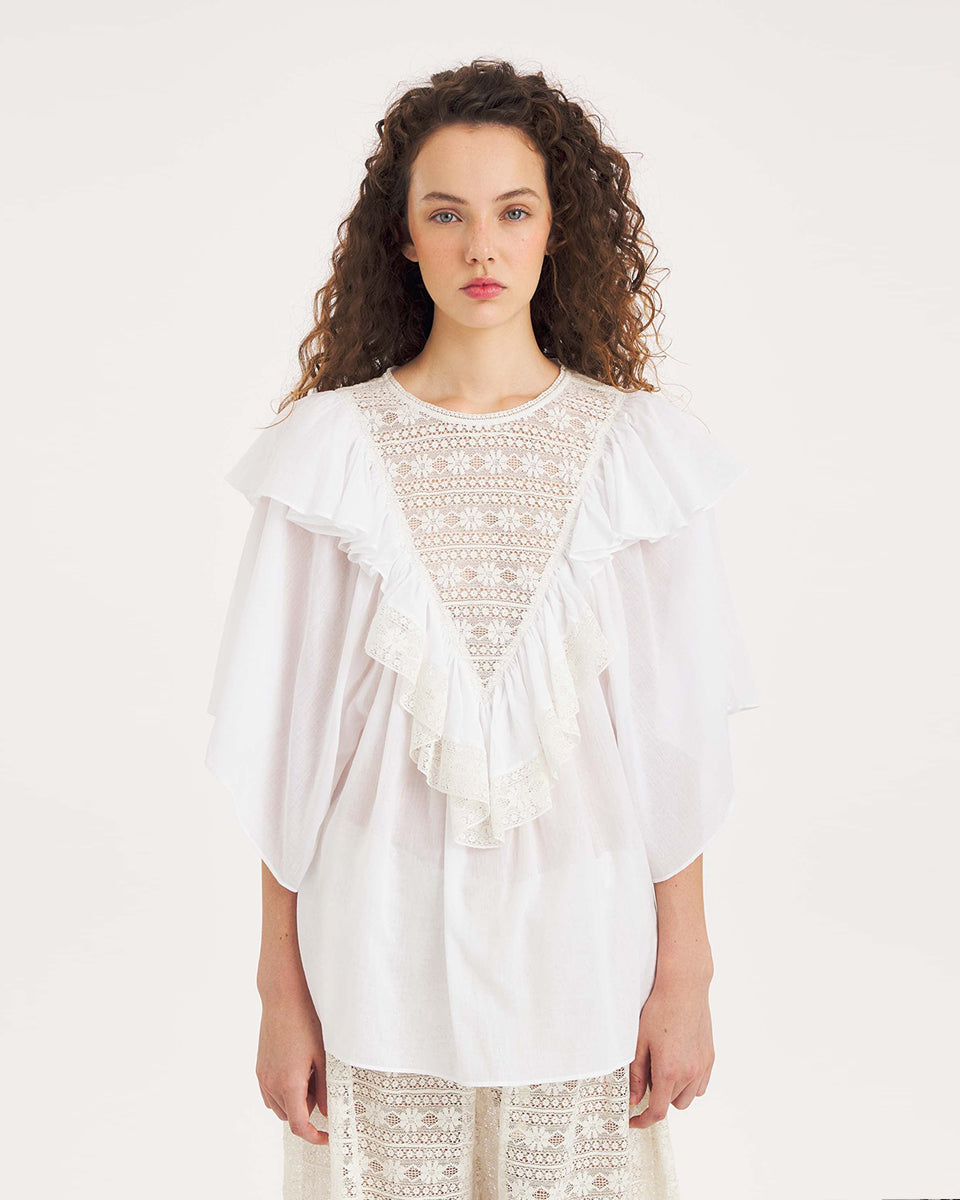 Luźna, biała bluzka Dolly White marki Antik Batik o swobodnym kroju, wyróżniającą się mocno romantycznym stylem boho. Z przodu jak i z tyłu posiada duży, ażurowy panel z misternej koronki o geometryczno- kwiatowym wzorze, który układa się w kształt litery V. Koronkowy dekolt zakończony jest szerokimi falbanami, które płynnie przechodzą w luźne, motylkowe rękawy o długości do łokcia. Z tyłu bluzka posiada subtelne rozcięcie w łezkę zapinane na guzik.
-Swobodny, luźny fason
-Falbany
-Koronka
-Zamów
