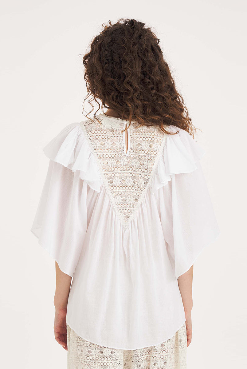 Luźna, biała bluzka Dolly White marki Antik Batik o swobodnym kroju, wyróżniającą się mocno romantycznym stylem boho. Z przodu jak i z tyłu posiada duży, ażurowy panel z misternej koronki o geometryczno- kwiatowym wzorze, który układa się w kształt litery V. Koronkowy dekolt zakończony jest szerokimi falbanami, które płynnie przechodzą w luźne, motylkowe rękawy o długości do łokcia. Z tyłu bluzka posiada subtelne rozcięcie w łezkę zapinane na guzik.
-Swobodny, luźny fason
-Falbany
-Koronka
-Zamów