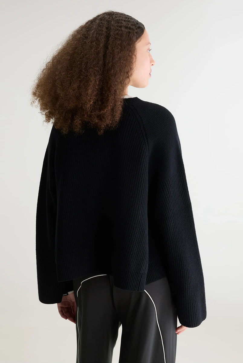 Luźny, krótki sweter z okrągłym dekoltem Dorou Black marki Bellerose wykonany z czarnej wełny merino, o średniej grubości dzianiny z panelami strukturalnymi. Posiada długie rękawy oraz ściągacze na mankietach i u dołu.
-Luźny krój: celowo powiększony, aby uzyskać obszerny wygląd.
-Krótszy fason