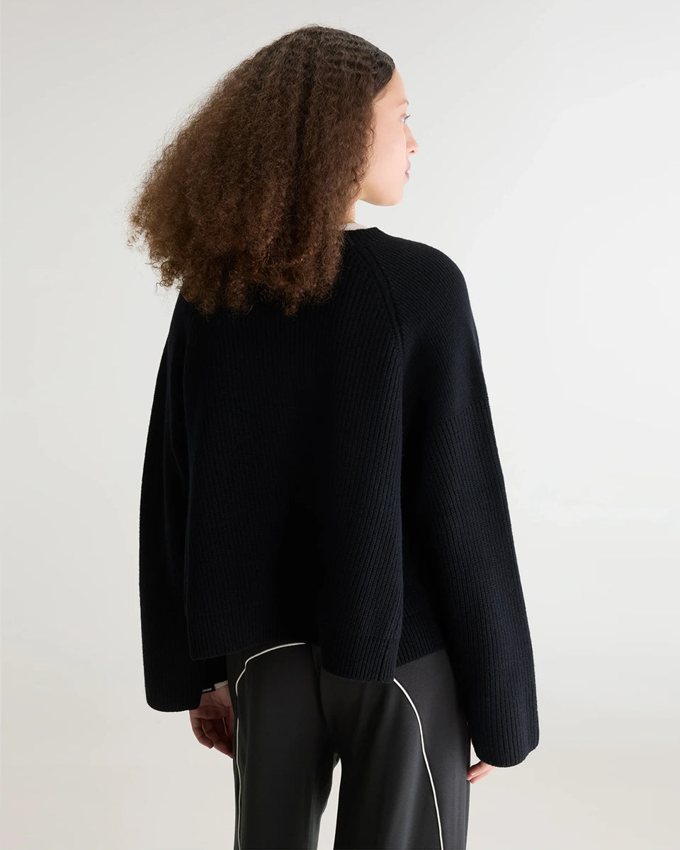 Luźny, krótki sweter z okrągłym dekoltem Dorou Black marki Bellerose wykonany z czarnej wełny merino, o średniej grubości dzianiny z panelami strukturalnymi. Posiada długie rękawy oraz ściągacze na mankietach i u dołu.
-Luźny krój: celowo powiększony, aby uzyskać obszerny wygląd.
-Krótszy fason