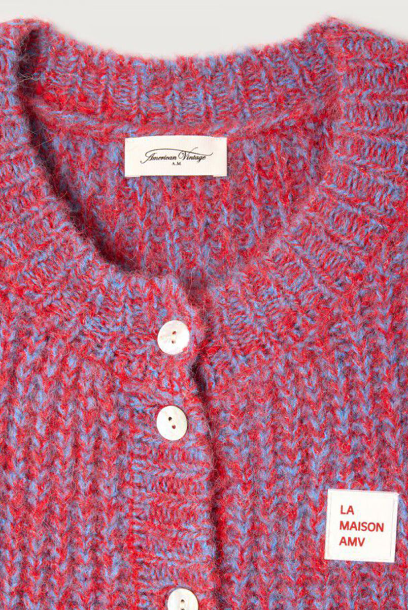 Krótki kardigan EAST19 Chili Red marki American Vintage bez rękawów, z okrągłym dekoltem i zapięciem na guziki. Posiada naszywkę z logo na piersi. Wyjątkowości i nowoczesności dodaje mu efekt uzyskany przez połączenie dwóch kontrastujących nici. Wykonany z puszystej dzianiny z alpaką i wełną. Niezbędny sweter, który można nosić samodzielnie lub na golf. 