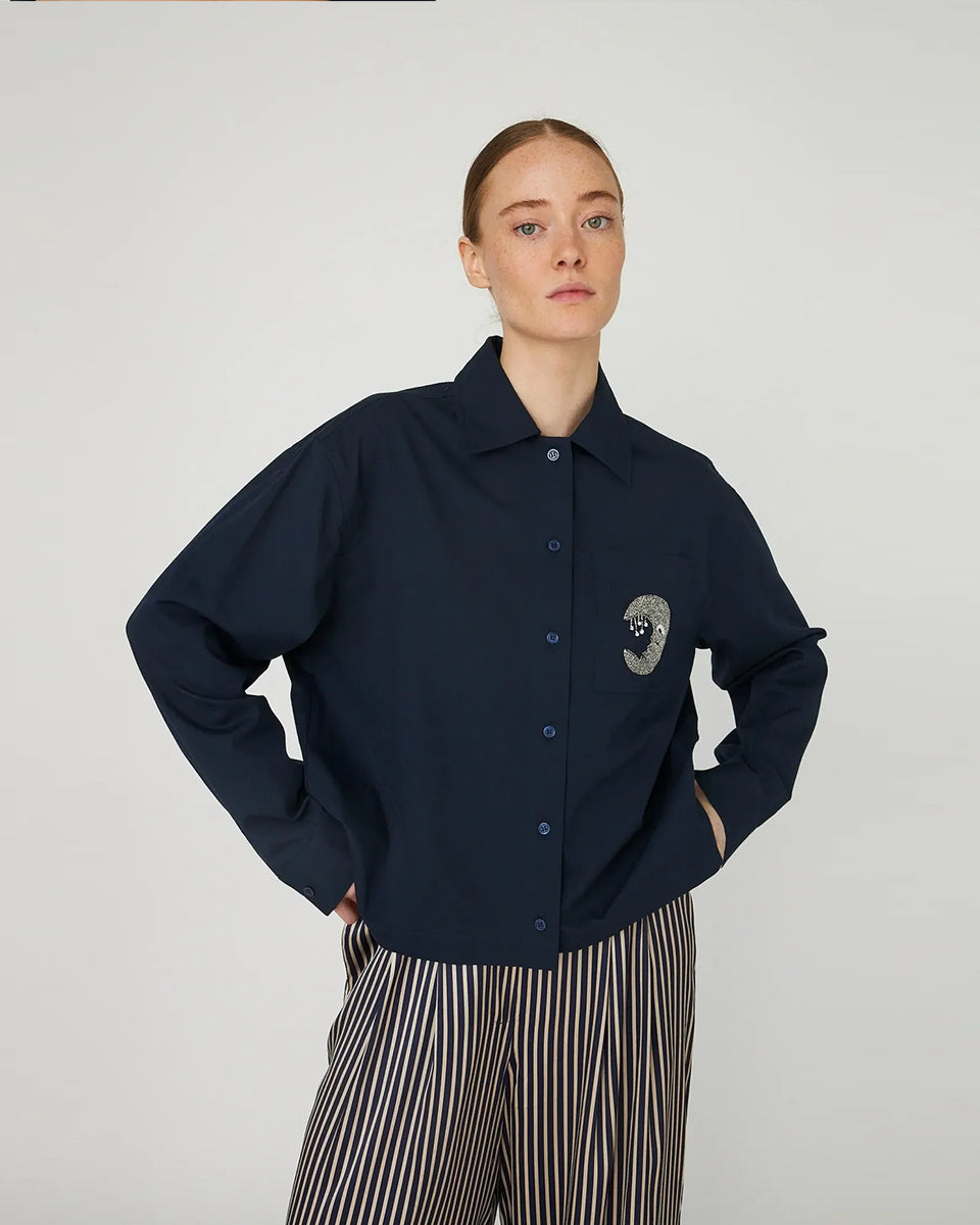 Luźna, granatowa koszula Embellished Moon Navy marki STELLA NOVA z długimi rękawami i mankietem. Ma klasyczny kołnierzyk i zapięcie na guziki z przodu. Na lewej piersi posiada kieszeń z wyhaftowanym księżycem. 