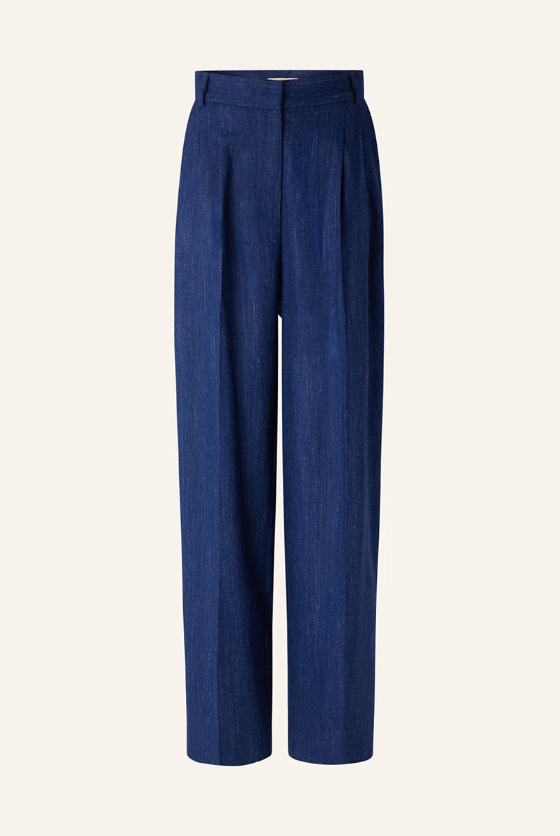 Niebieskie spodnie Emile Queen Blue francuskiej marki Sessun z wysokim stanem, z zakładkami w talii, uszyte z eleganckiej flaneli z melanżowej przędzy. Mają zapięcie na suwak z wewnętrznym haftem, kieszenie skośne z przodu i kieszenie z patką z tyłu. Przez całą długość nogawki widoczne są wyraźne kanty. 