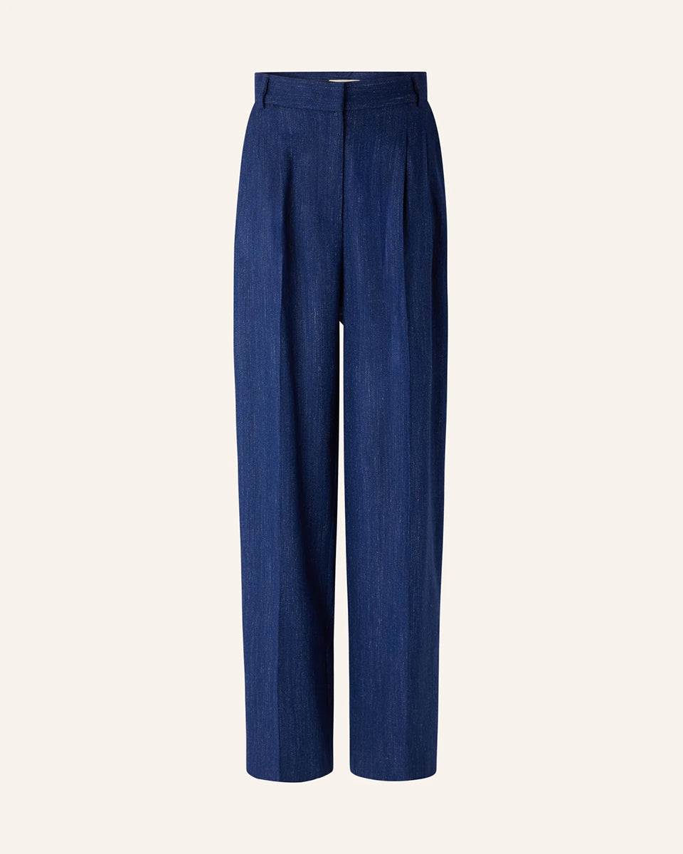 Niebieskie spodnie Emile Queen Blue francuskiej marki Sessun z wysokim stanem, z zakładkami w talii, uszyte z eleganckiej flaneli z melanżowej przędzy. Mają zapięcie na suwak z wewnętrznym haftem, kieszenie skośne z przodu i kieszenie z patką z tyłu. Przez całą długość nogawki widoczne są wyraźne kanty. 