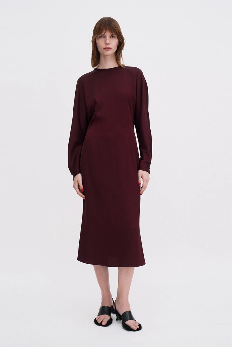 Minimalistyczna, luźna, elegancka sukienka midi Filippa K z okrągłym dekoltem i długimi rękawami rozszerzanymi pod pachami z guzikami przy mankietach. Na plecach posiada długie, wąskie rozcięcie. Z tyłu przy szyi zapinana na jeden guzik. Lekko zwężana w talii. Z tyłu w pasie ma elastyczną gumkę.