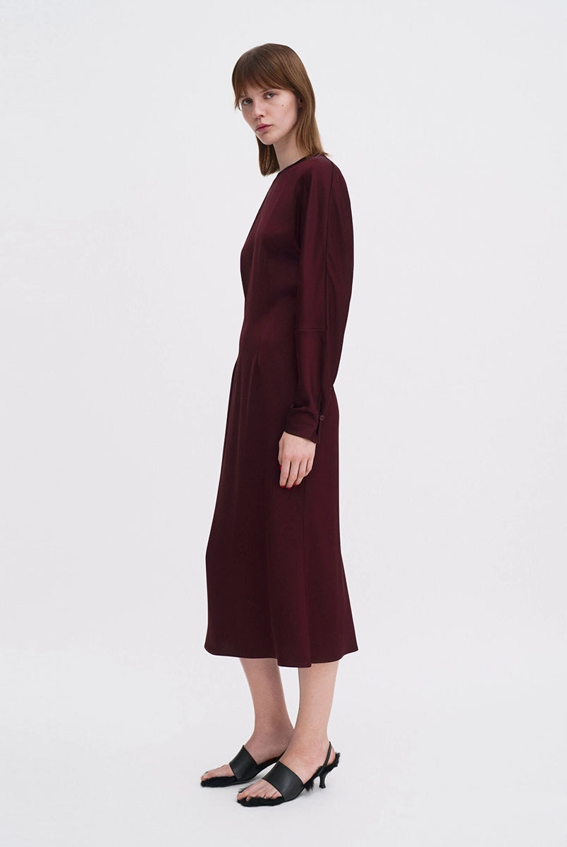 Minimalistyczna, luźna, elegancka sukienka midi Filippa K z okrągłym dekoltem i długimi rękawami rozszerzanymi pod pachami z guzikami przy mankietach. Na plecach posiada długie, wąskie rozcięcie. Z tyłu przy szyi zapinana na jeden guzik. Lekko zwężana w talii. Z tyłu w pasie ma elastyczną gumkę.