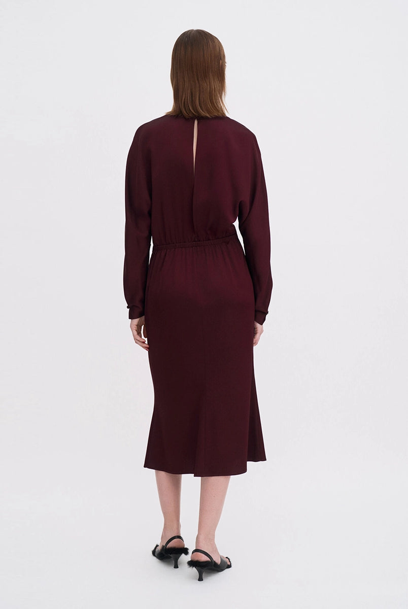Minimalistyczna, luźna, elegancka sukienka midi Filippa K z okrągłym dekoltem i długimi rękawami rozszerzanymi pod pachami z guzikami przy mankietach. Na plecach posiada długie, wąskie rozcięcie. Z tyłu przy szyi zapinana na jeden guzik. Lekko zwężana w talii. Z tyłu w pasie ma elastyczną gumkę.