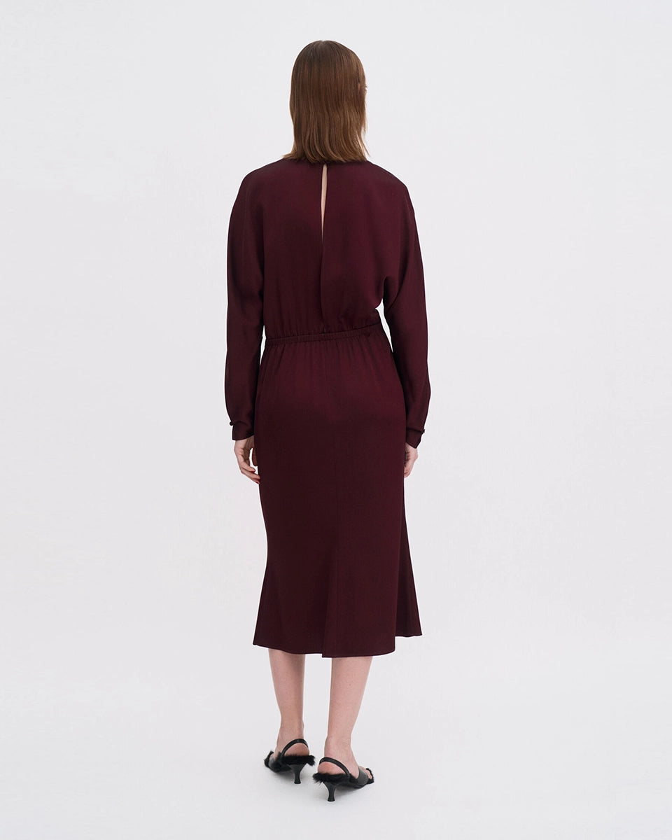 Minimalistyczna, luźna, elegancka sukienka midi Filippa K z okrągłym dekoltem i długimi rękawami rozszerzanymi pod pachami z guzikami przy mankietach. Na plecach posiada długie, wąskie rozcięcie. Z tyłu przy szyi zapinana na jeden guzik. Lekko zwężana w talii. Z tyłu w pasie ma elastyczną gumkę.