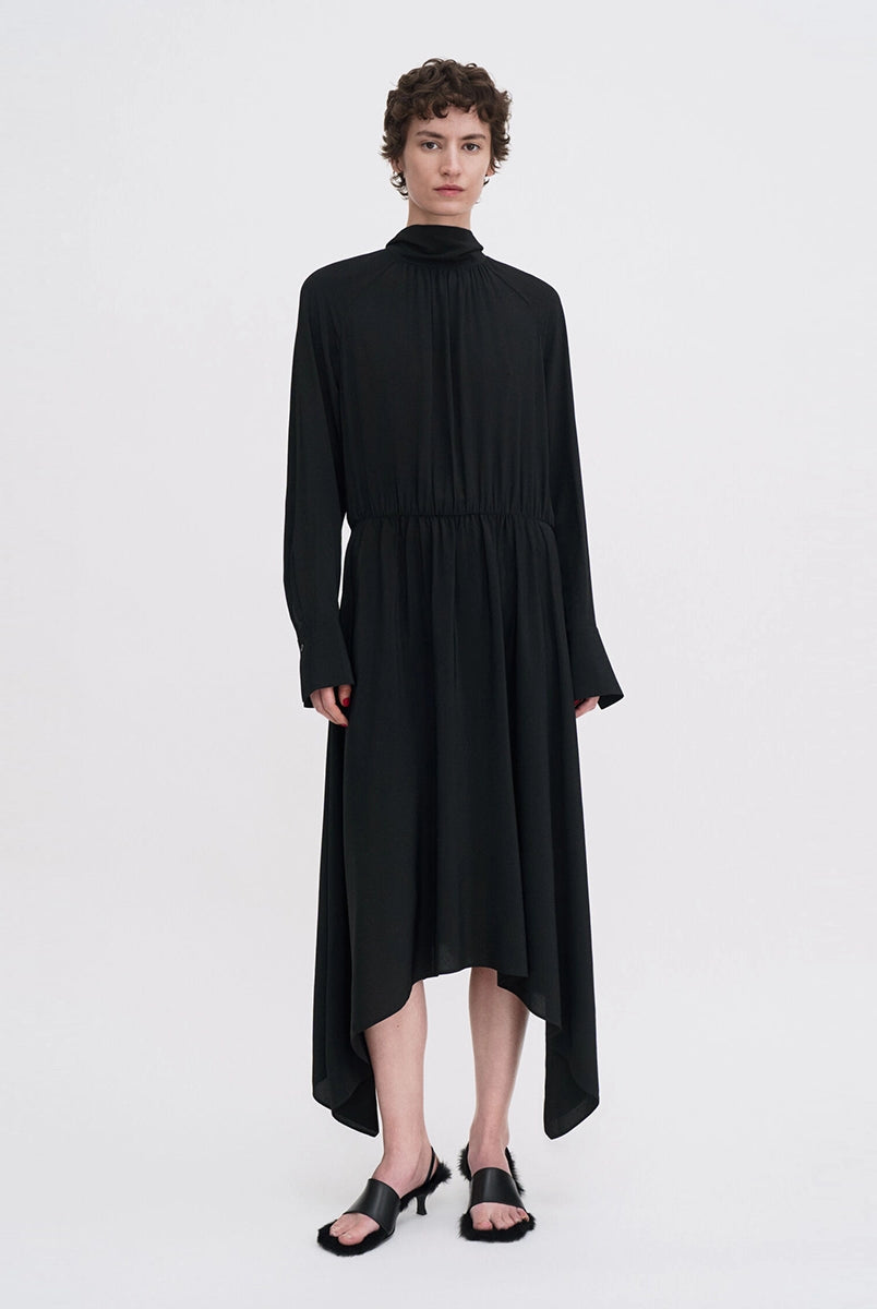 Minimalistyczna, luźna, elegancka sukienka midi Filippa K z wysokim dekoltem w formie golfu i wiązaniem z tyłu przy szyi. Sukienka ma długie rękawy zakończone mankietami oraz efektowne, wąskie rozcięcie na plecach. Z przodu marszczona przy dekolcie i i talii. U dołu wykończona asymetrycznie