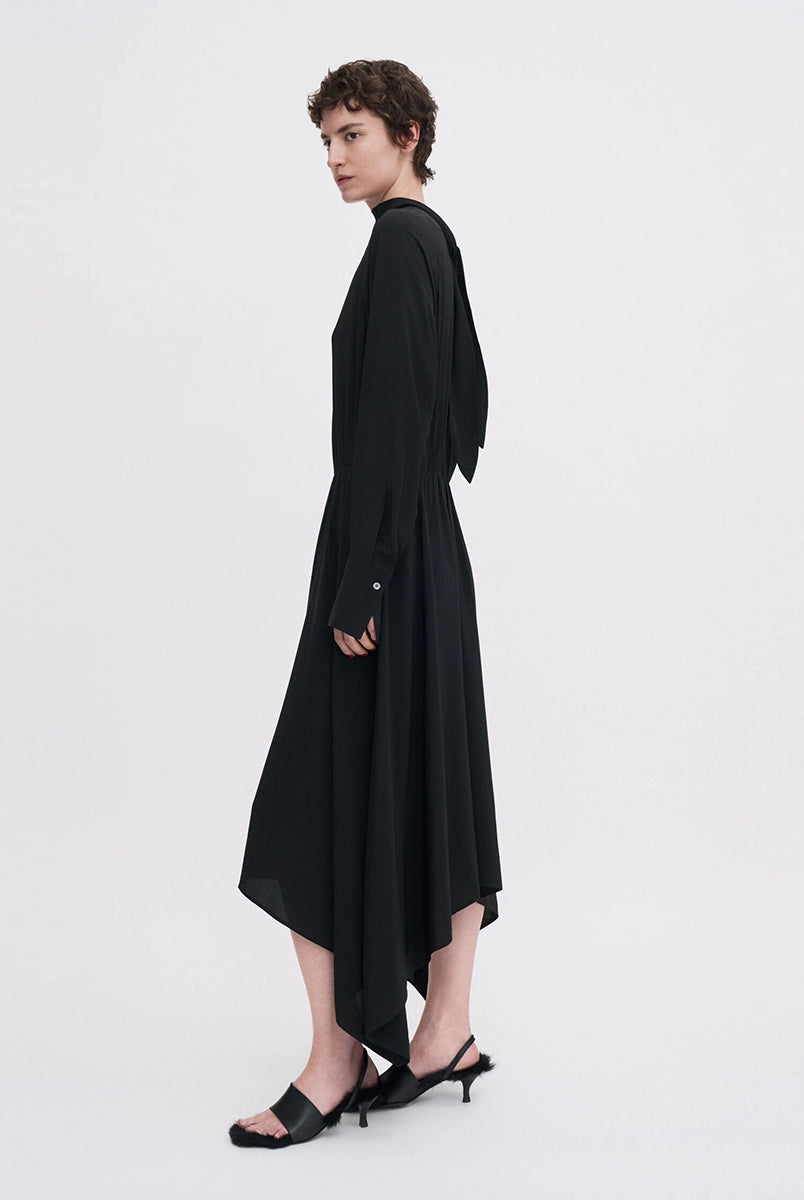 Minimalistyczna, luźna, elegancka sukienka midi Filippa K z wysokim dekoltem w formie golfu i wiązaniem z tyłu przy szyi. Sukienka ma długie rękawy zakończone mankietami oraz efektowne, wąskie rozcięcie na plecach. Z przodu marszczona przy dekolcie i i talii. U dołu wykończona asymetrycznie