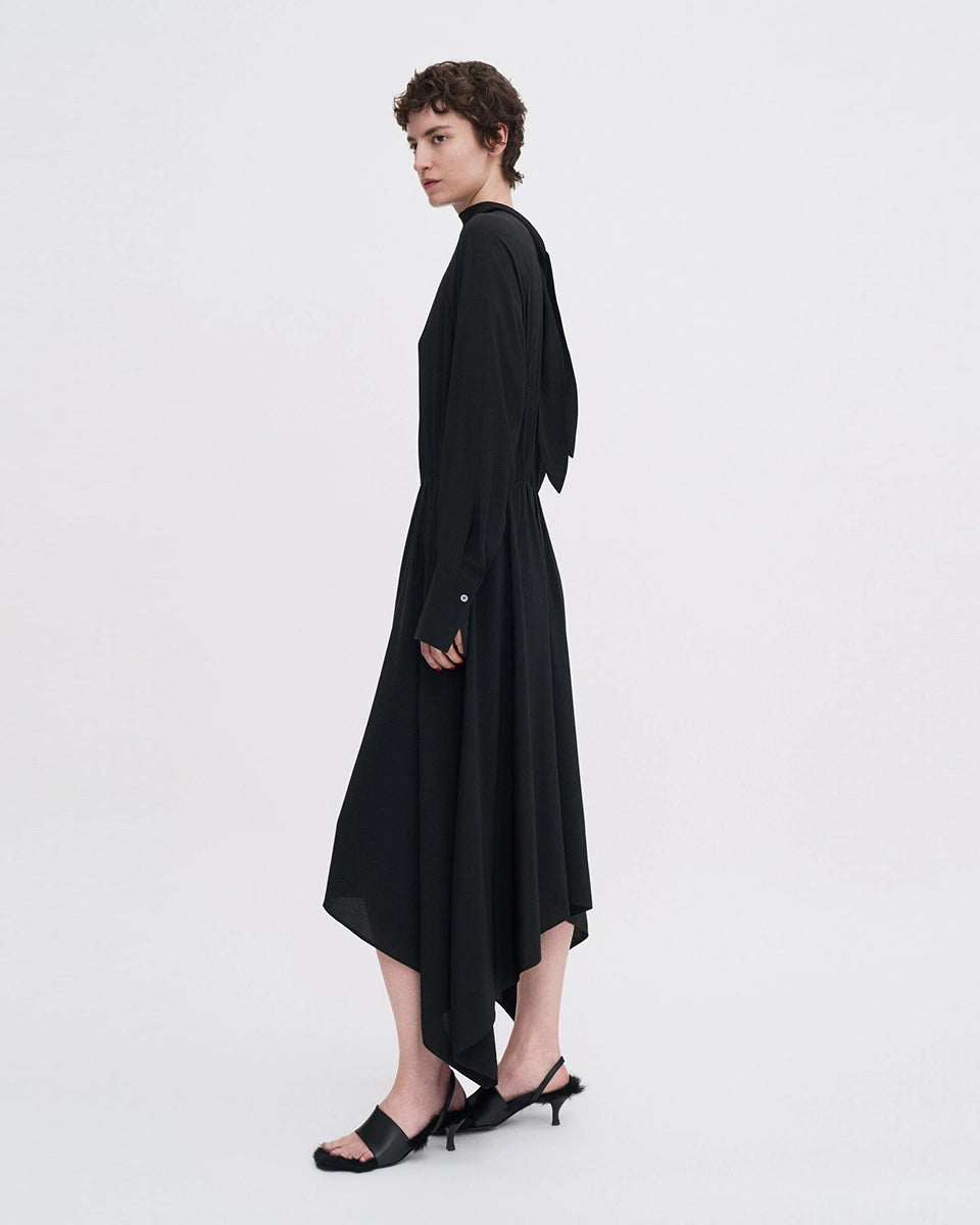 Minimalistyczna, luźna, elegancka sukienka midi Filippa K z wysokim dekoltem w formie golfu i wiązaniem z tyłu przy szyi. Sukienka ma długie rękawy zakończone mankietami oraz efektowne, wąskie rozcięcie na plecach. Z przodu marszczona przy dekolcie i i talii. U dołu wykończona asymetrycznie