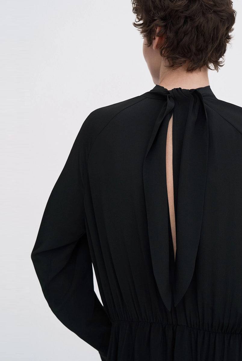 Minimalistyczna, luźna, elegancka sukienka midi Filippa K z wysokim dekoltem w formie golfu i wiązaniem z tyłu przy szyi. Sukienka ma długie rękawy zakończone mankietami oraz efektowne, wąskie rozcięcie na plecach. Z przodu marszczona przy dekolcie i i talii. U dołu wykończona asymetrycznie