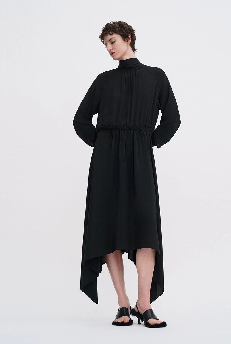 Minimalistyczna, luźna, elegancka sukienka midi Filippa K z wysokim dekoltem w formie golfu i wiązaniem z tyłu przy szyi. Sukienka ma długie rękawy zakończone mankietami oraz efektowne, wąskie rozcięcie na plecach. Z przodu marszczona przy dekolcie i i talii. U dołu wykończona asymetrycznie