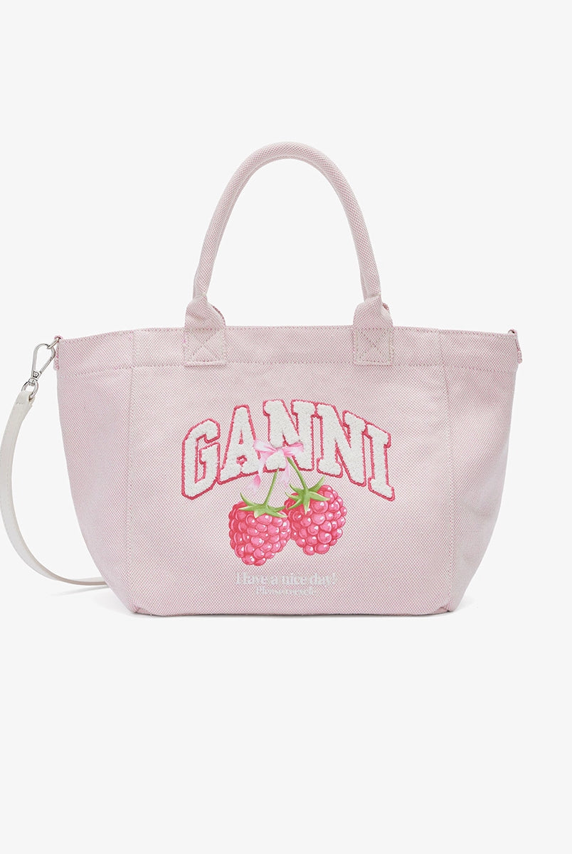 Średniej wielkości, trapezowa, różowa torba shopper 2110 Rasperry GANNI z pluszowym logo marki oraz z uroczym printem z motywem malin. Torba posiada dwie, grube, krótkie rączki do wygodnego trzymania w dłoni oraz odpinany, cienki, długi pasek do wygodnego zawiedzenia na ramieniu. Wewnątrz znajduje się mała kieszonka zapinana na zamek błyskawiczny. Wykonana z grubego, sztywnego, płóciennego materiału. 