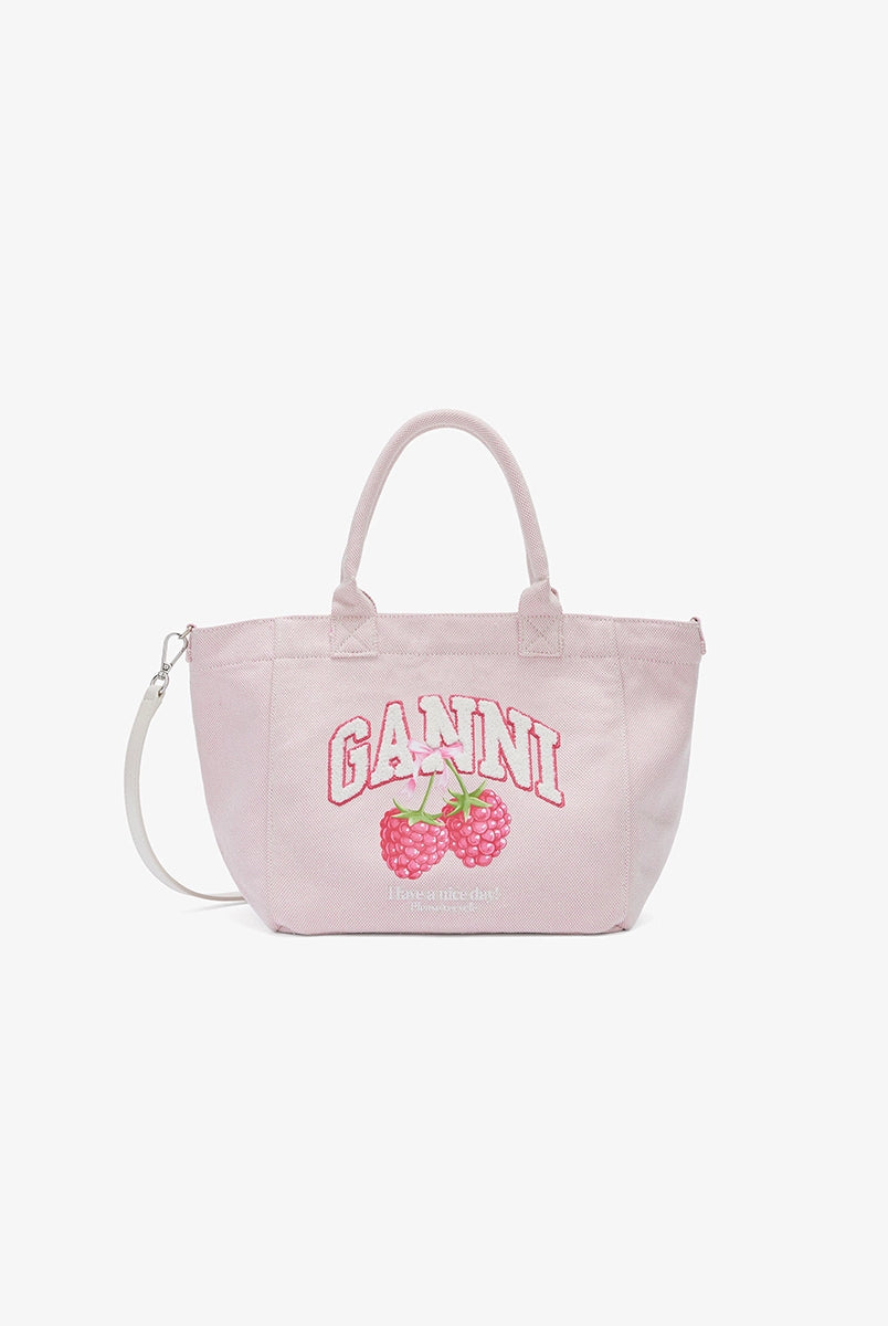 Mała, trapezowa, różowa torba shopper 2110 Rasperry GANNI z pluszowym logo marki oraz z uroczym printem z motywem malin. Torba posiada dwie, grube, krótkie rączki do wygodnego trzymania w dłoni oraz odpinany, cienki, długi pasek do wygodnego zawiedzenia na ramieniu. Wewnątrz znajduje się mała kieszonka zapinana na zamek błyskawiczny. Wykonana z grubego, sztywnego, płóciennego materiału.
