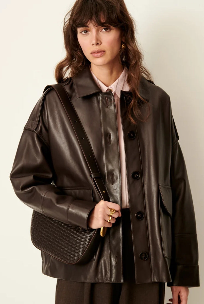Brązowa, luźna kurtka Harriboyd Coffee Leather francuskiej marki Sessun w stylu klasycznej pilotki. Wykonana jest z gładkiej, ciemnobrązowej skóry o lekkim połysku. Z przodu zapinana jest na duże, czarne guziki, a po bokach ma duże naszywane kieszenie. Rękawy są długie, z mankietami zapinanymi na guzik