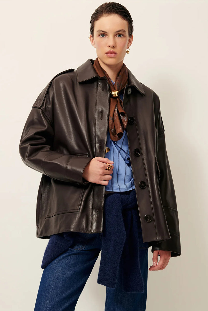 Brązowa, luźna kurtka Harriboyd Coffee Leather francuskiej marki Sessun w stylu klasycznej pilotki. Wykonana jest z gładkiej, ciemnobrązowej skóry o lekkim połysku. Z przodu zapinana jest na duże, czarne guziki, a po bogach ma duże naszywane kieszenie. Rękawy są długie, z mankietami zapinanymi na guzik. Tył kurtki jest prosty, z poziomym szwem przez plecy i elastycznym ściągaczem w dolnej części. 